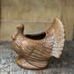 A ceramic turkey-shaped planter in a warm brown glazed finish, sitting on a rustic wooden surface with a wooden background.