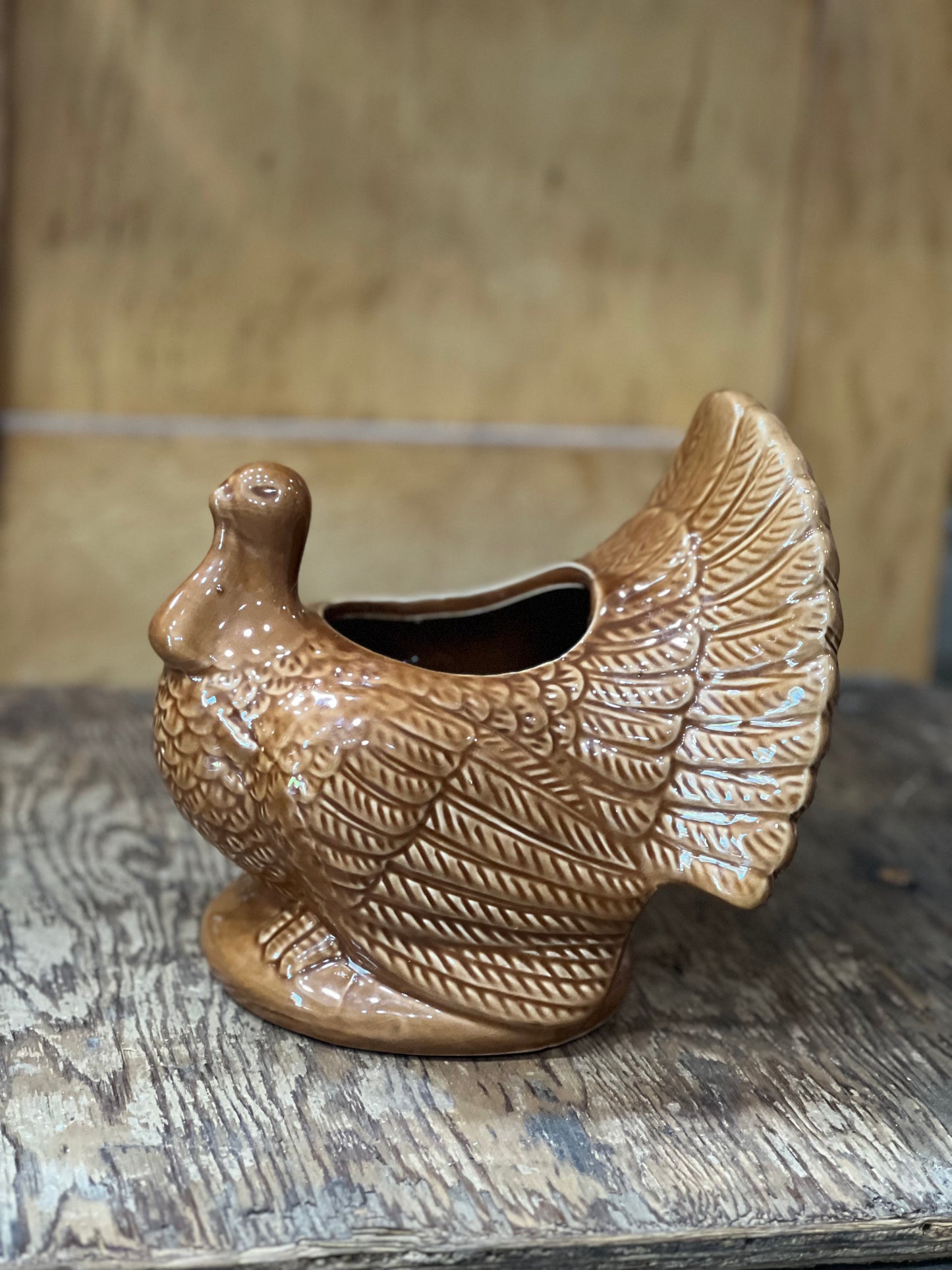 A ceramic turkey-shaped planter in a warm brown glazed finish, sitting on a rustic wooden surface with a wooden background.