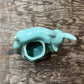 A small glossy ceramic animal-shaped vessel, shaped like a rabbit or hare with a hollow center, in a light aqua glaze, placed on a rustic wooden surface.