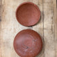 Two round terracotta clay bowls, one shown from the top and one from the bottom side, placed on a rustic wooden plank surface.
