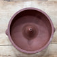 A terracotta-colored clay pot or planter shown from a top-down perspective on a rustic wooden plank surface.