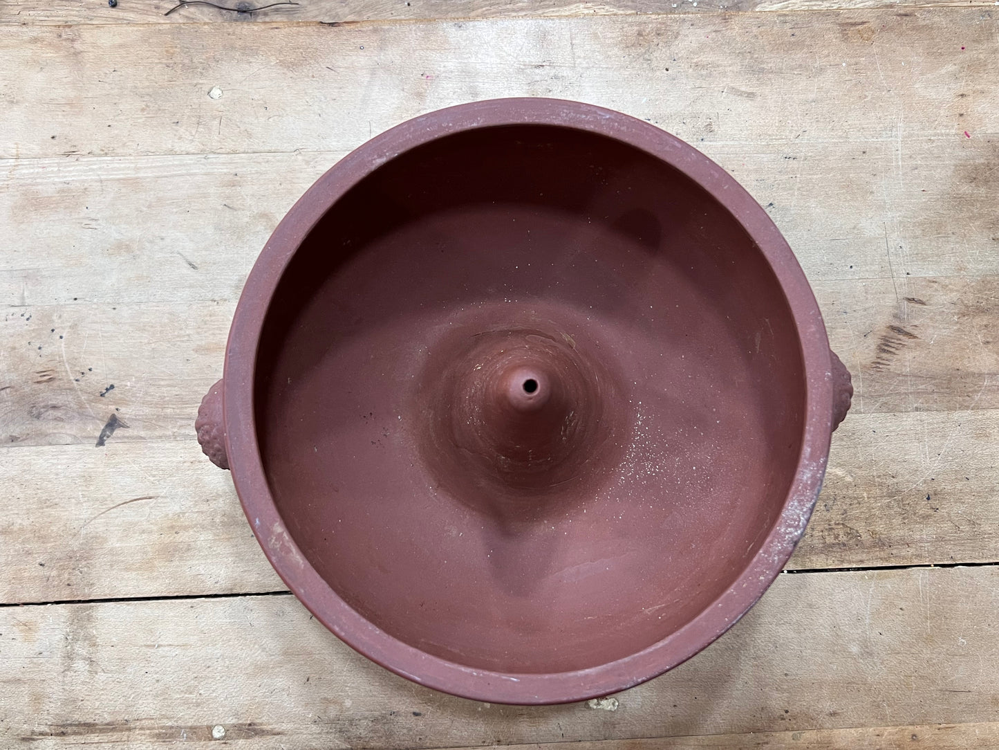 A terracotta-colored clay pot or planter shown from a top-down perspective on a rustic wooden plank surface.
