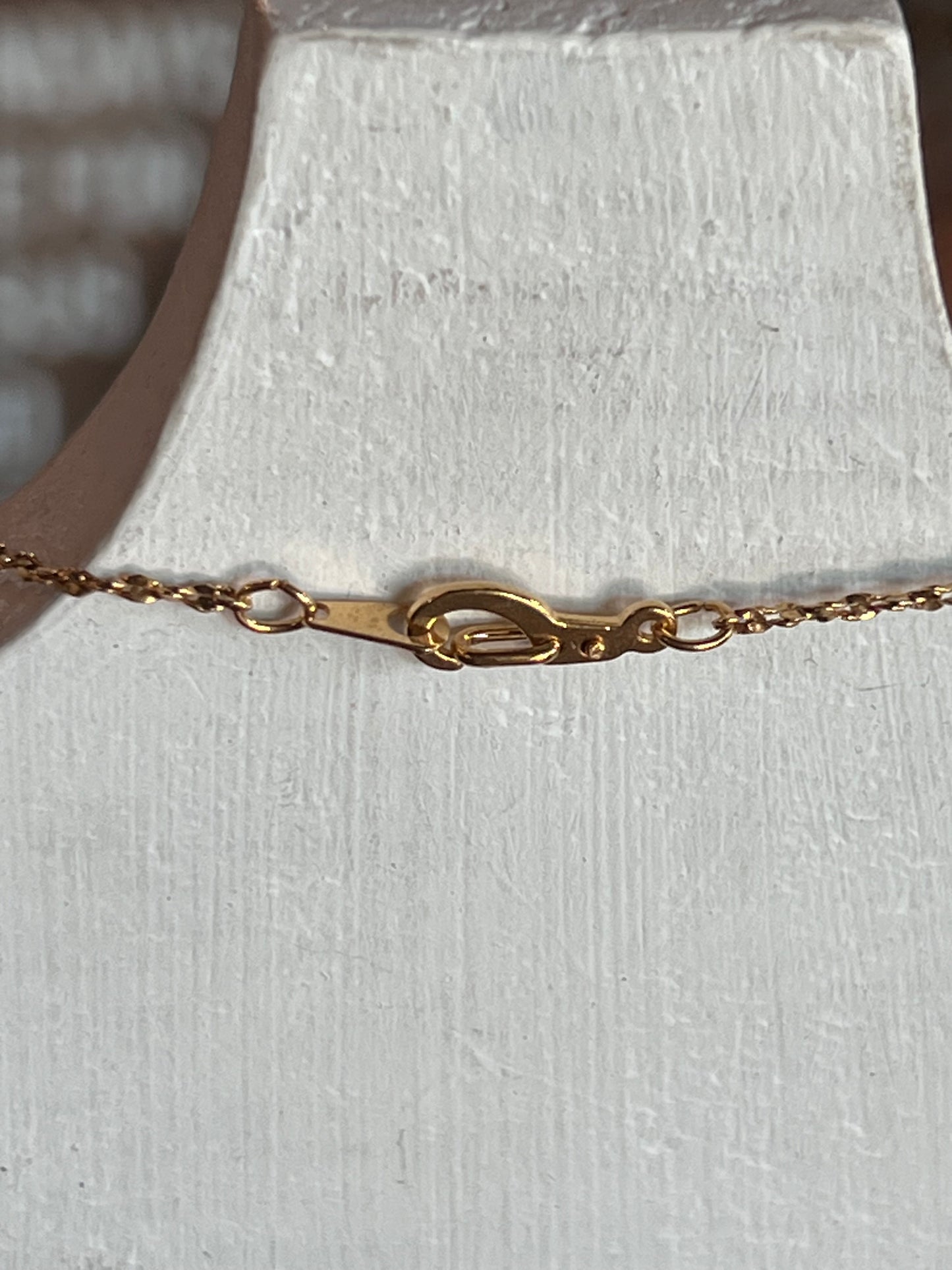 Close-up of a gold chain necklace with a lobster clasp, displayed on a textured white jewelry bust.