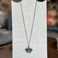 A silver crown pendant necklace with turquoise-colored stones, displayed on a white wooden stand.