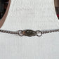 A silver chain bracelet with a textured, organic-shaped centerpiece and two small rings, displayed on a white textured bust.