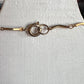 A close-up of a gold-toned metal chain bracelet or necklace with a lobster clasp and interlocking ring detail, displayed on a textured white surface.