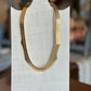 A gold-toned chain necklace with a textured, segmented scale design, displayed on a white fabric-covered mannequin bust.