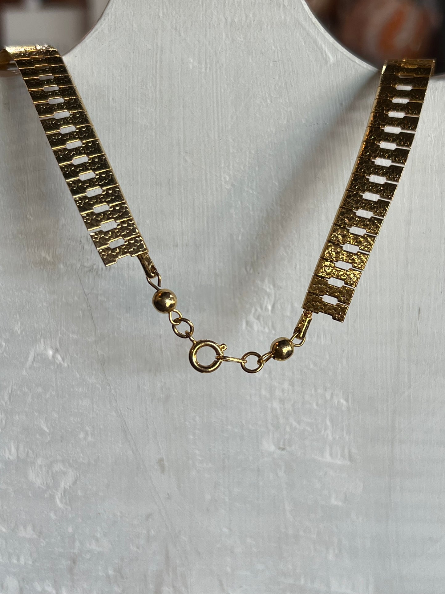A textured gold-tone chain link necklace displayed on a white mannequin bust, featuring a lobster clasp closure.