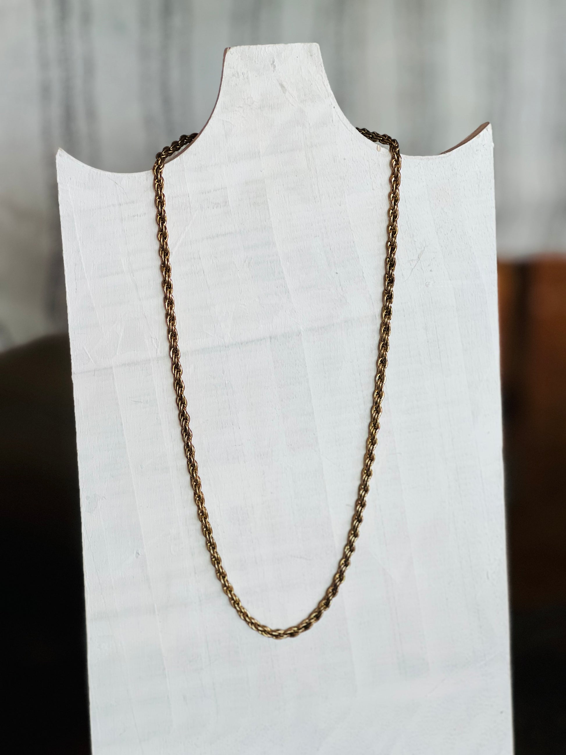 A twisted rope chain necklace in a bronze finish, displayed on a white fabric-covered jewelry bust.