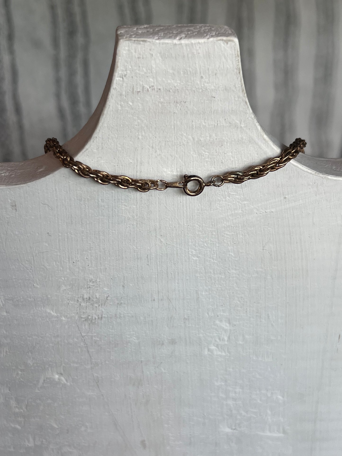 A dark bronze twisted chain link bracelet with a spring ring clasp, displayed on a white painted wooden jewelry bust.