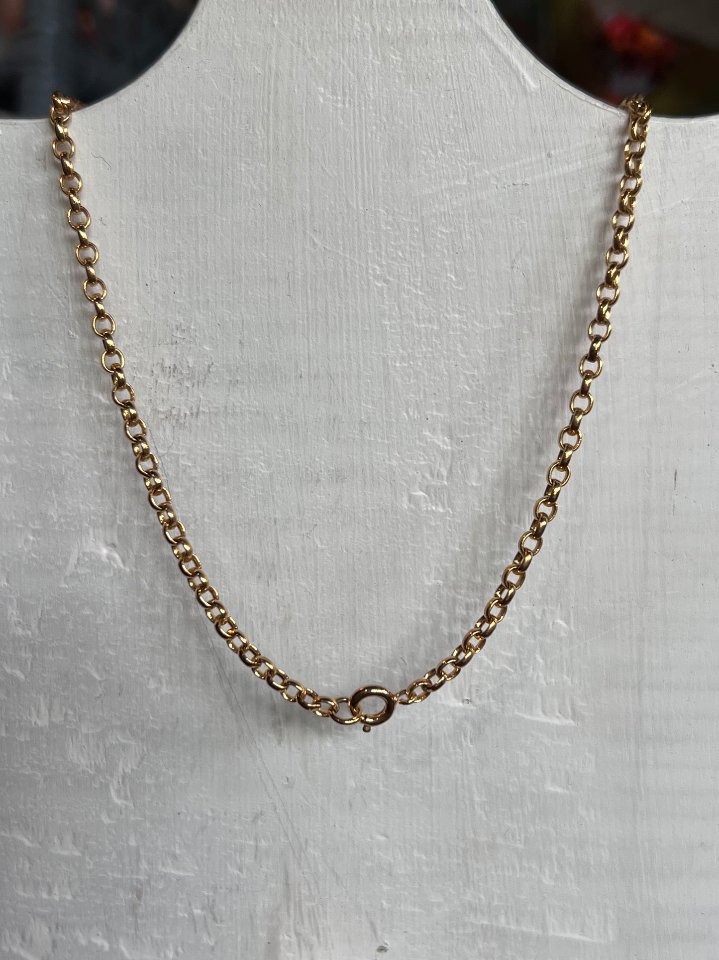 A gold chain necklace with a small ring clasp, displayed on a white textured bust form.