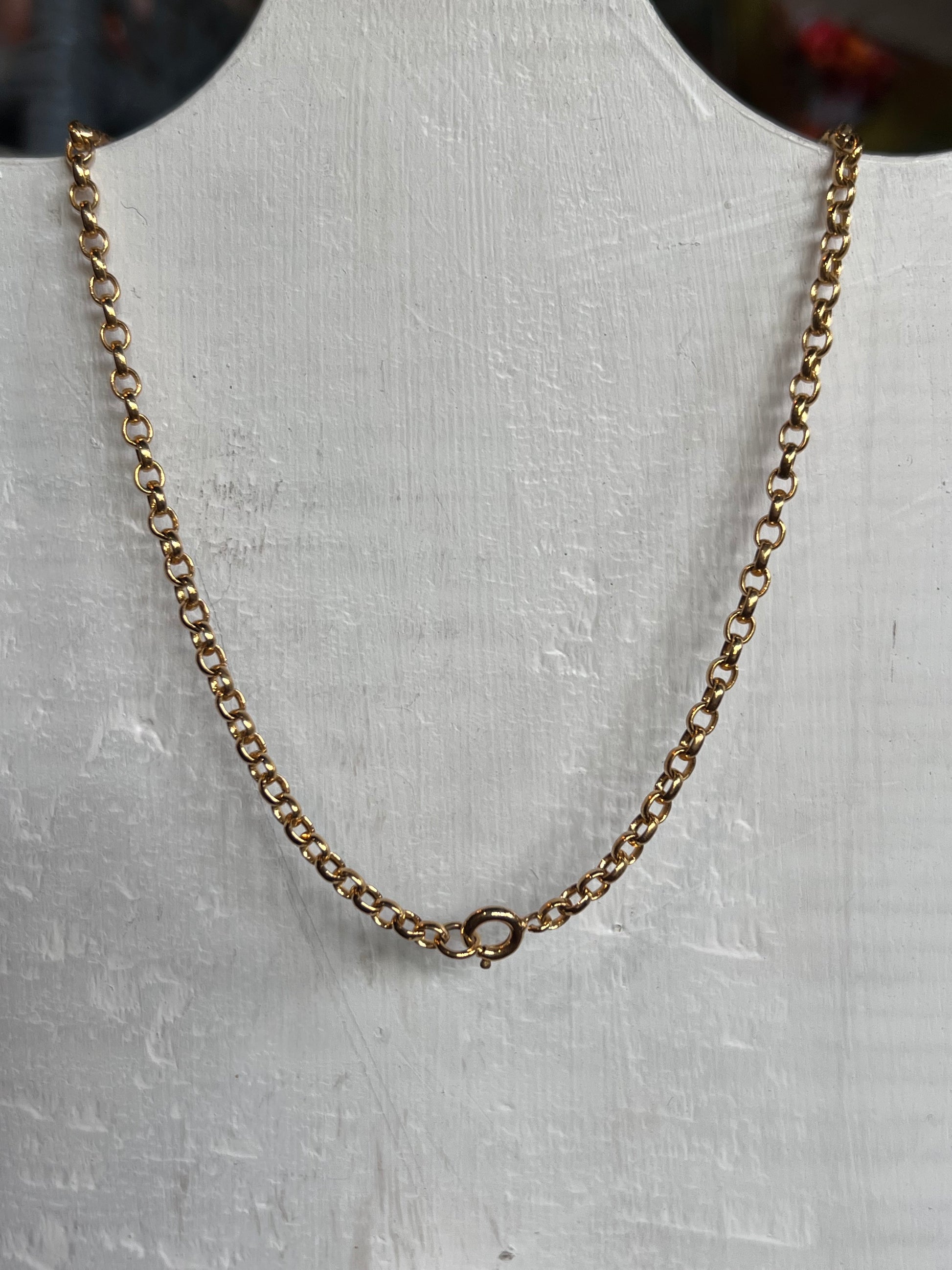 A gold chain necklace with a small ring clasp, displayed on a white textured bust form.