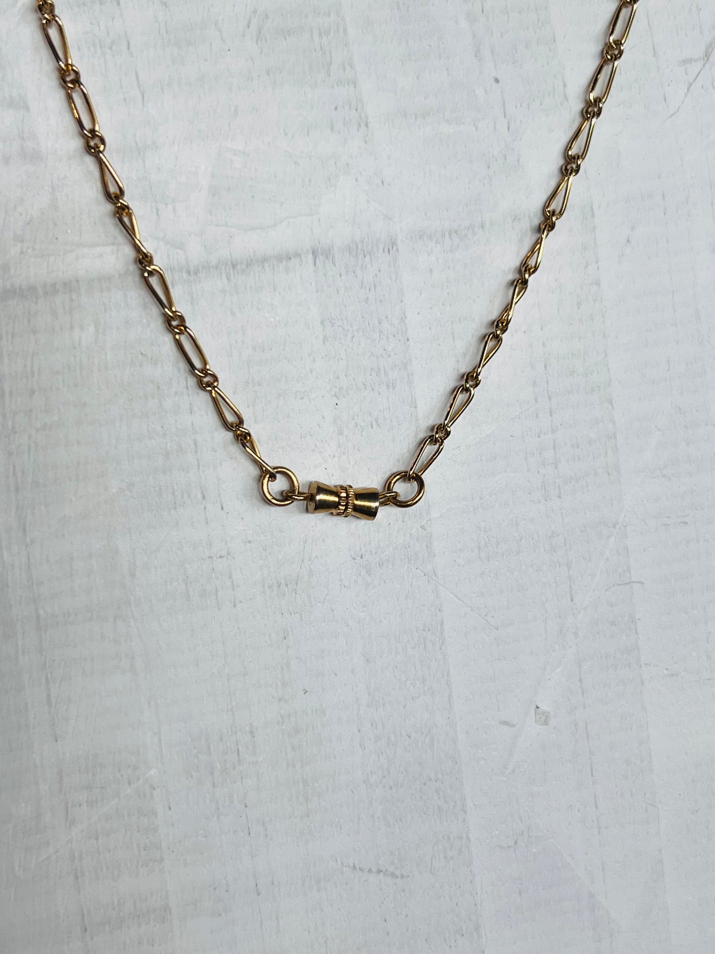 A gold-toned chain necklace with a central clasp, laid flat on a light gray textured surface.