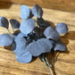 A cluster of artificial dusty blue-gray hydrangea-like leaves on a thin stem, displayed on a wooden tabletop.