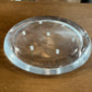 A clear, round acrylic or glass trivet with six small raised feet, shown on a wooden tabletop.