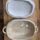 Two ceramic casserole dishes with scalloped edges and side handles, one stacked inside the other, displayed on a rustic wooden surface.