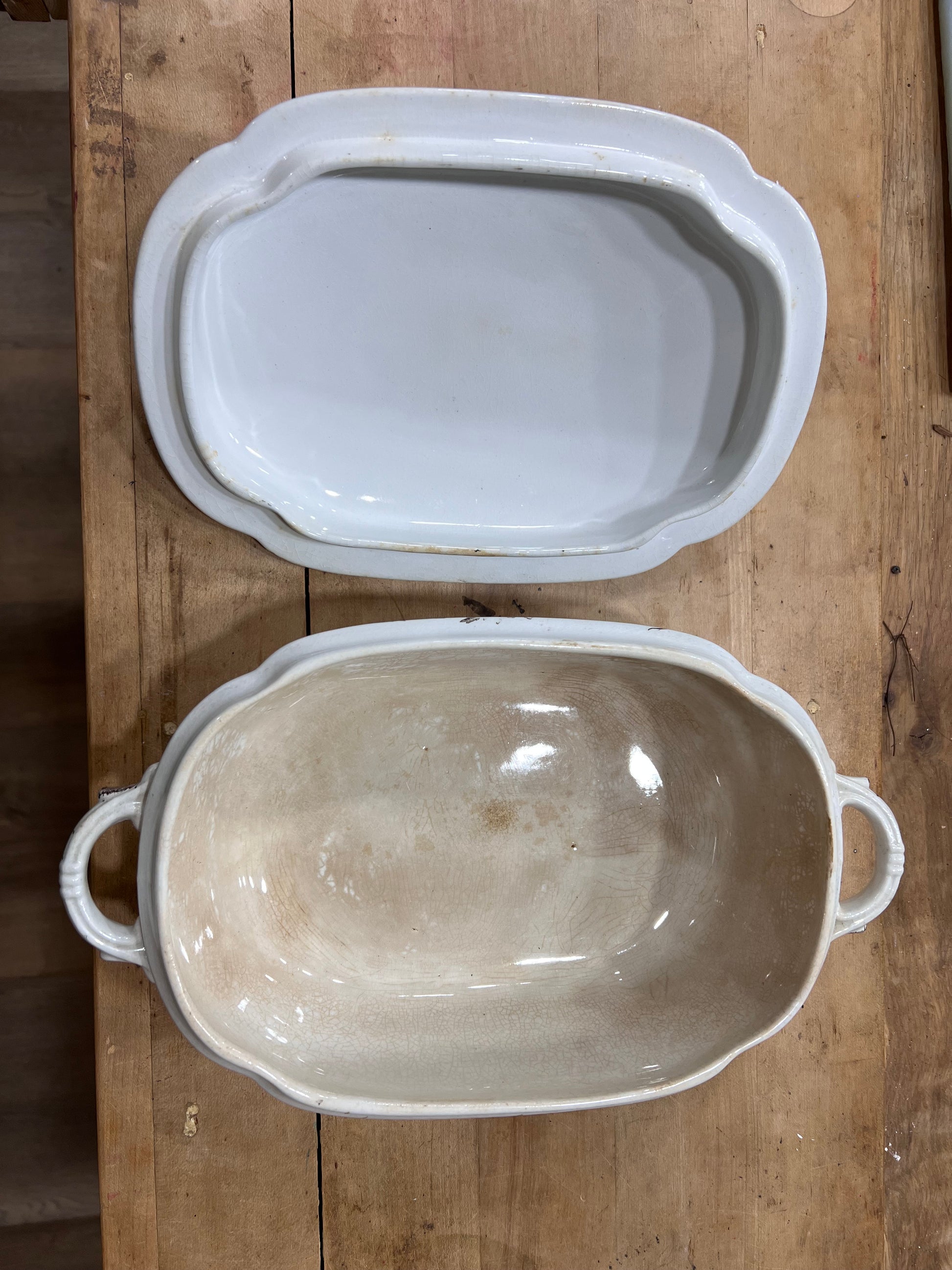 Two ceramic casserole dishes with scalloped edges and side handles, one stacked inside the other, displayed on a rustic wooden surface.