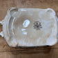 An antique ceramic baking dish shown from the bottom, featuring a glossy off-white glaze, two side handles, and a central black printed 'ESSEX' brand mark, placed on a rustic wooden surface.