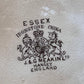 Close-up of a light beige textured surface with a black printed crest and text reading 'ESSEX IRONSTONE CHINA' and 'J.&G MEAKIN' LTD HANLEY ENGLAND'.