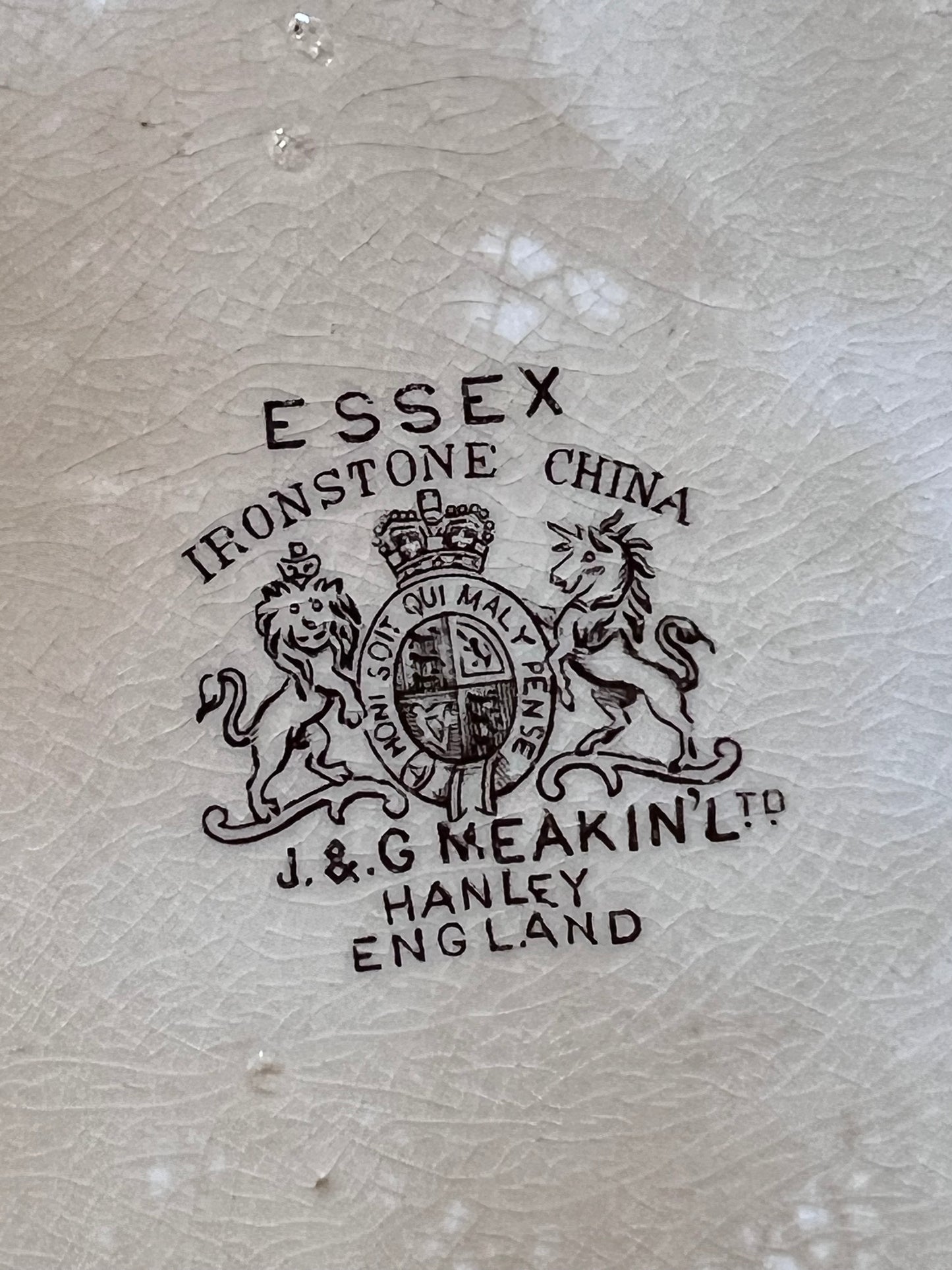 Close-up of a light beige textured surface with a black printed crest and text reading 'ESSEX IRONSTONE CHINA' and 'J.&G MEAKIN' LTD HANLEY ENGLAND'.