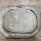 An antique oval ceramic dish or tray with a raised rim, shown from a top-down perspective on a wooden surface. The glaze is a warm, distressed cream-beige color with a dark printed brand label near the top edge that reads 'BURLINGTON'.