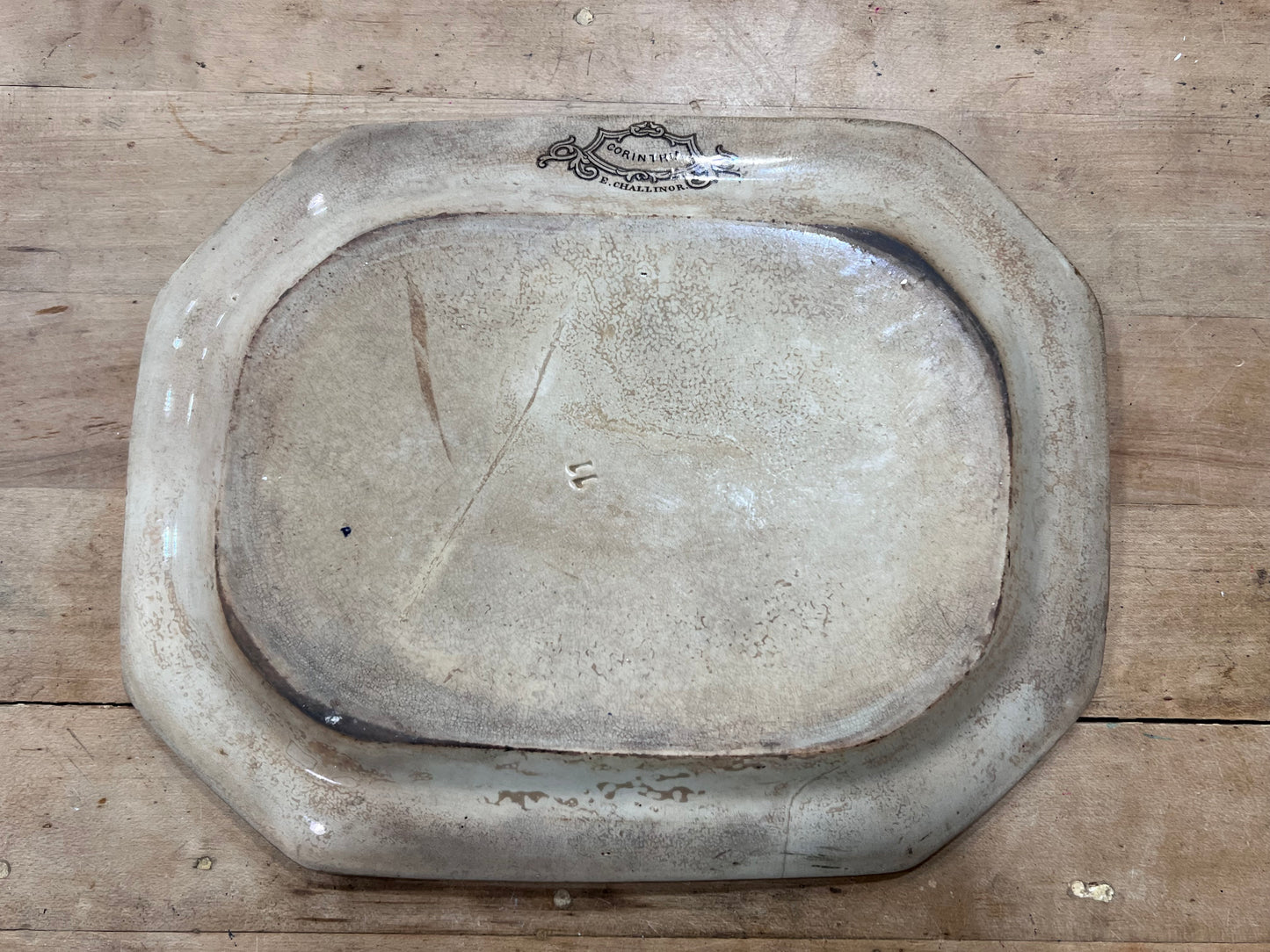 An antique oval ceramic dish or tray with a raised rim, shown from a top-down perspective on a wooden surface. The glaze is a warm, distressed cream-beige color with a dark printed brand label near the top edge that reads 'BURLINGTON'.