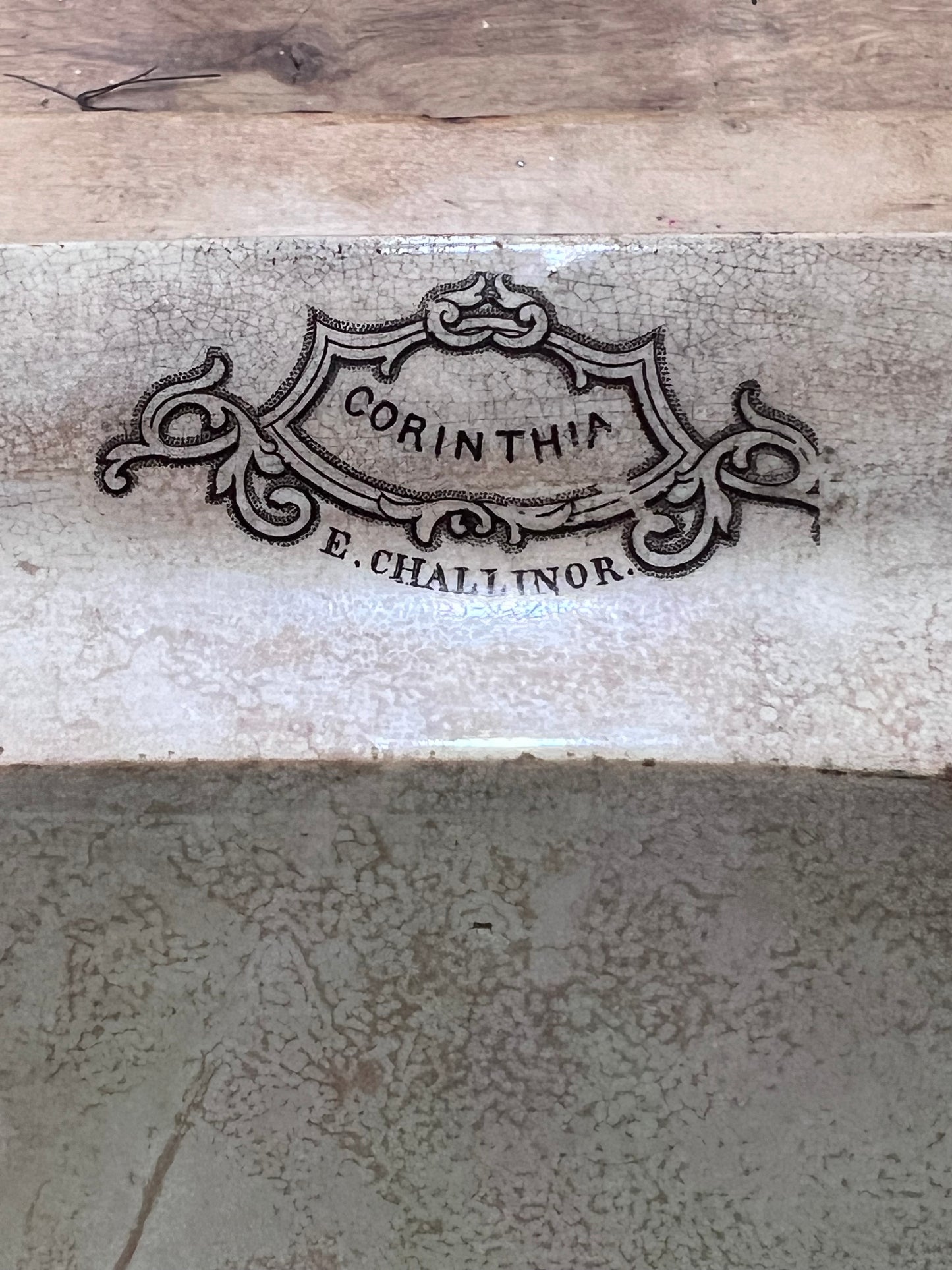 Close-up of a ceramic tile or stone surface with a decorative embossed or printed crest reading “CORINTHIA” and “E. CHALLINOR.