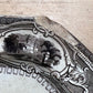 A close-up of a vintage ceramic plate or dish fragment with a black printed landscape scene and ornate border, resting on a light wood surface.