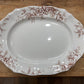An oval white ceramic serving platter with a brown floral border pattern, photographed from above on a rustic wooden surface.