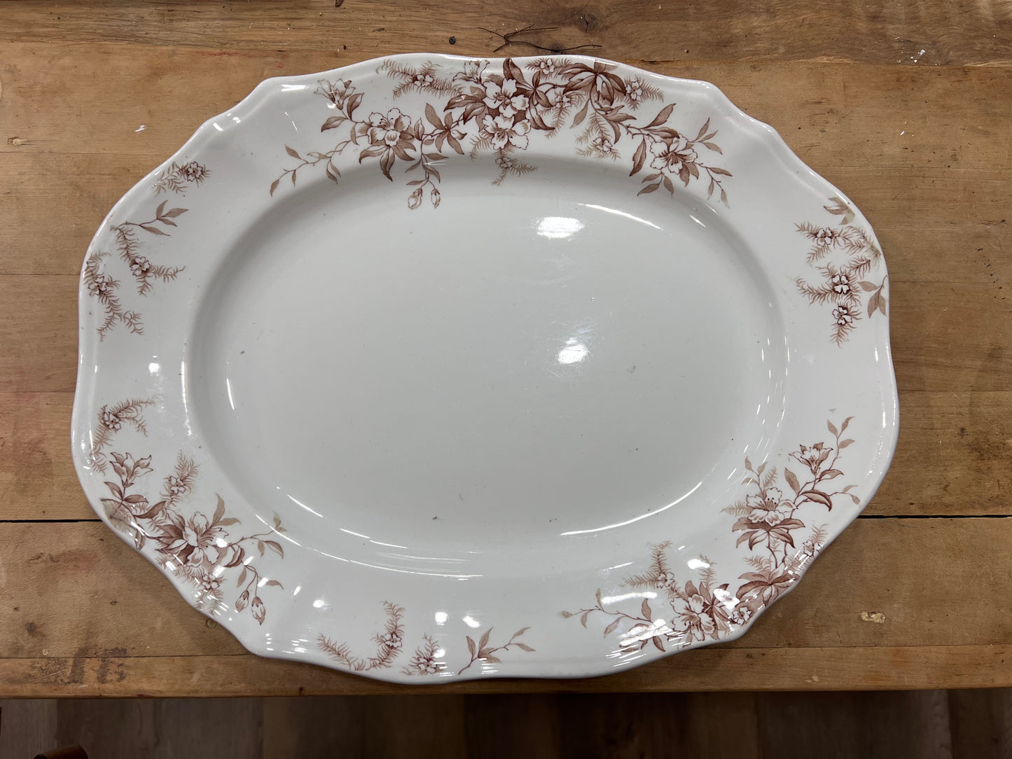 An oval white ceramic serving platter with a brown floral border pattern, photographed from above on a rustic wooden surface.