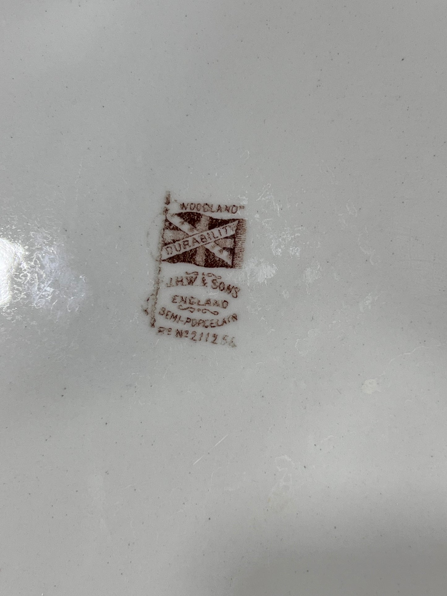 Close-up of a white porcelain surface showing a brown J.H.W. Sons Woodland Durability stamp.