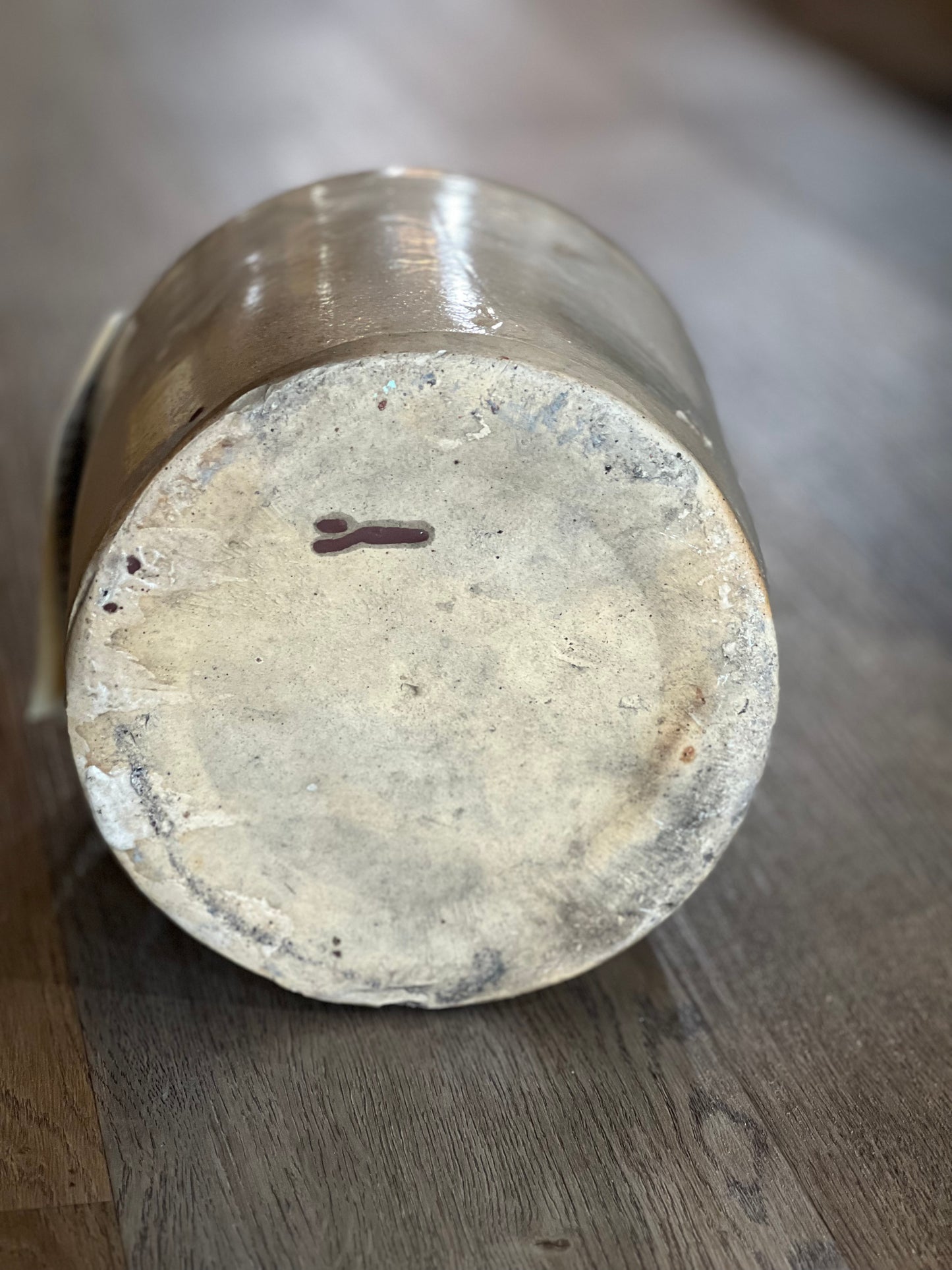 A close-up shot of the bottom base of a cylindrical ceramic pot or planter, showing a textured, dusty off-white clay surface with a small dark mark, resting on a dark wood floor.