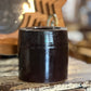 A dark brown glazed ceramic cup or candle holder with a glossy finish, sitting on a distressed wooden surface with a warm, blurred background.