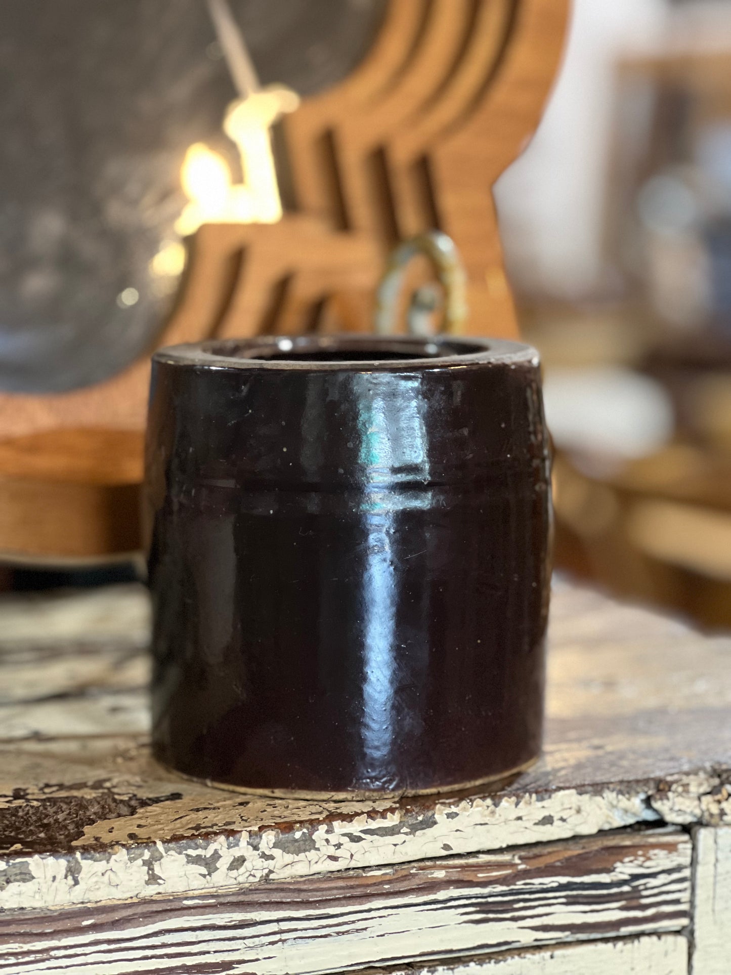 A dark brown glazed ceramic cup or candle holder with a glossy finish, sitting on a distressed wooden surface with a warm, blurred background.