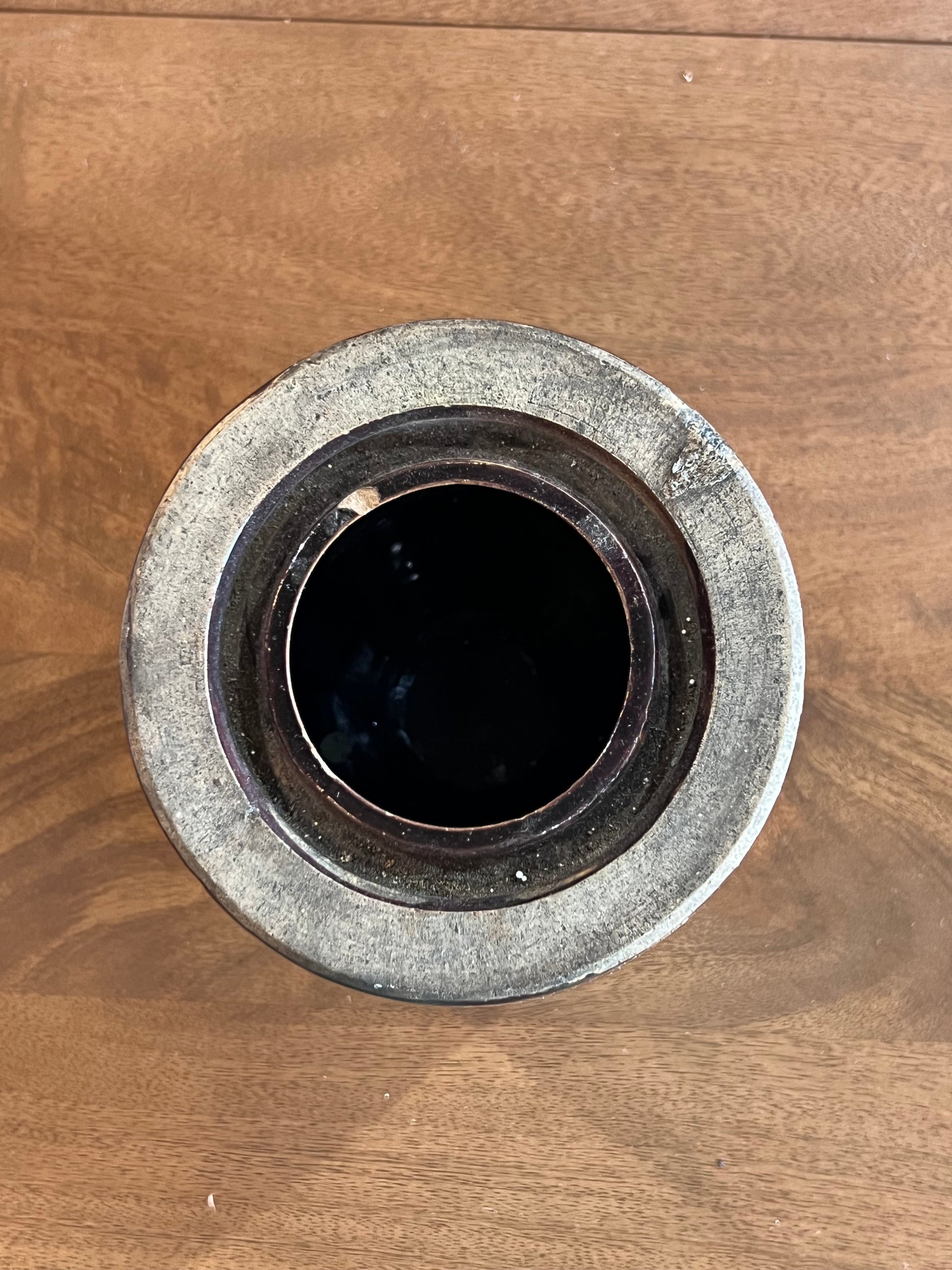 A round, rustic ceramic pot or planter with a textured gray and white glaze, photographed from directly above on a brown wooden surface.