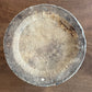 A round, rustic wooden bowl or dish with a weathered, textured surface, photographed from directly above on a brown wooden tabletop.