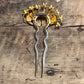A vintage gold and silver filigree hair pin with a crown-like top and two long twisted stems, displayed on a rustic wooden surface.
