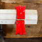 A glossy red decorative wall hook or hanging ornament with a small gold-toned metal accent, shown mounted on a light wood dowel against a rustic wooden background.