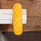 A thick, glossy yellow twisted bangle bracelet displayed on a light-colored wooden stand against a rustic dark wood background.