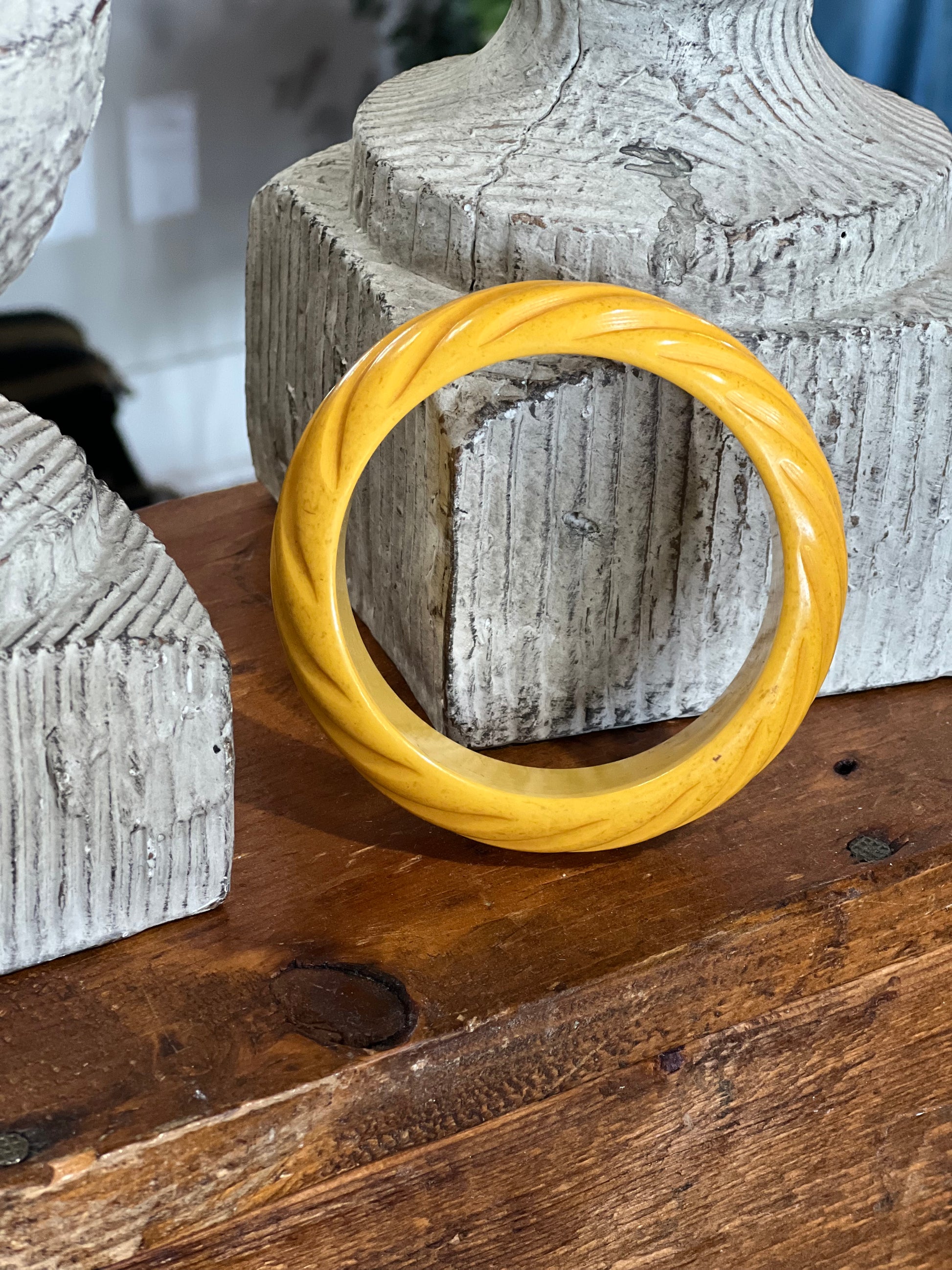 A twisted yellow bangle bracelet displayed on a rustic wooden surface in front of textured gray stone props.