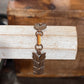 A vintage bronze-toned metal bracelet with a wheat or leaf cluster charm, displayed on a light-colored wooden block.