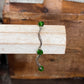 A silver-toned curved barbell nose ring with three faceted green gemstones, displayed on a light-colored wooden block against a rustic wooden background.