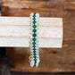 A beaded stretch bracelet with alternating dark green and clear faceted beads, displayed on a rustic white-painted wooden dowel with a wooden box in the background.