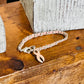 A silver-toned chain bracelet with a pink awareness ribbon charm, displayed on a rustic wooden surface next to a white textured block.