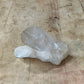 A raw, semi-translucent white crystal cluster resting on a worn, light-brown wooden tabletop.