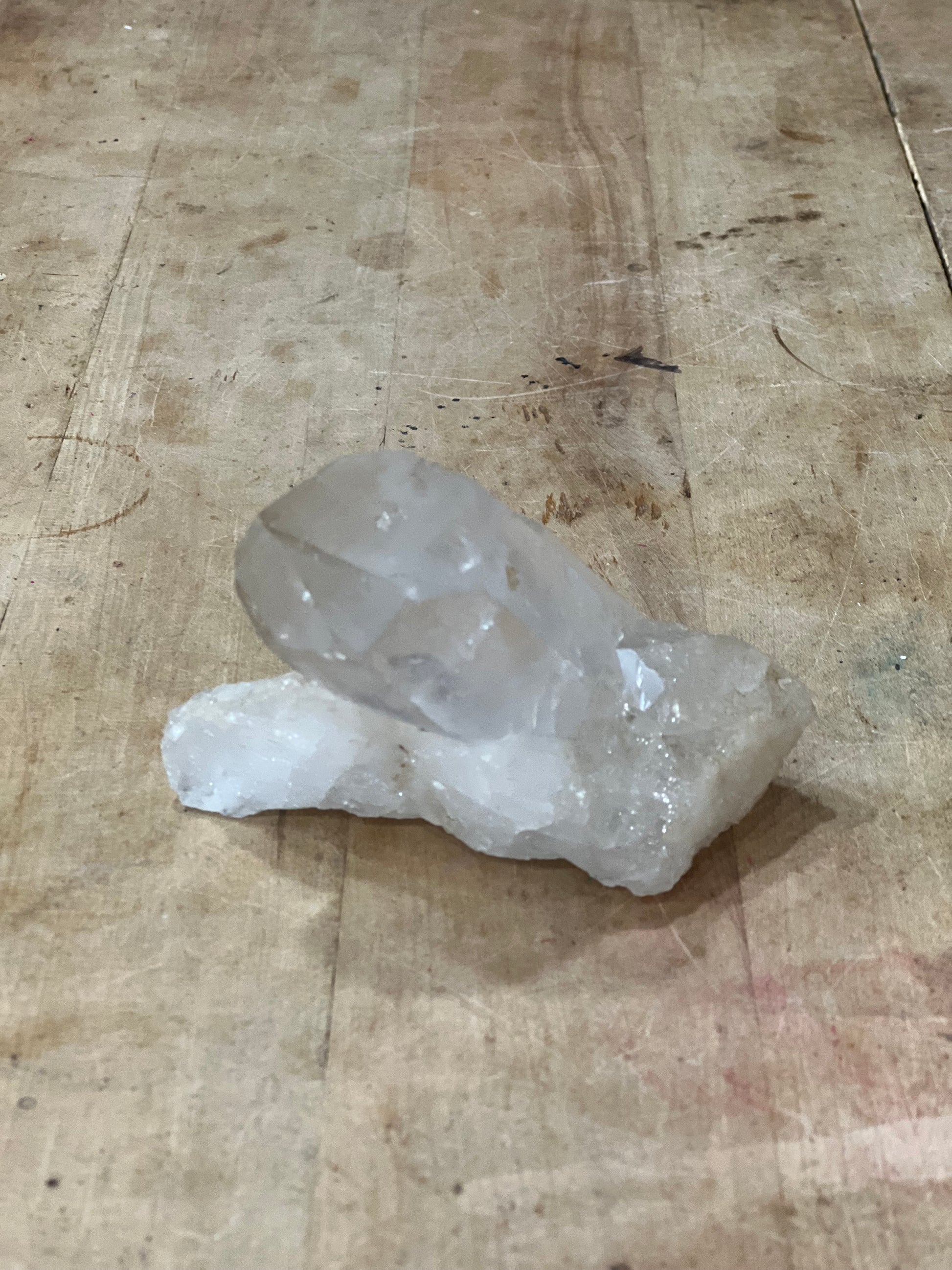 A raw, semi-translucent white crystal cluster resting on a worn, light-brown wooden tabletop.
