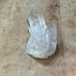 A natural clear quartz crystal cluster with rough and polished sections, resting on a weathered wooden surface.