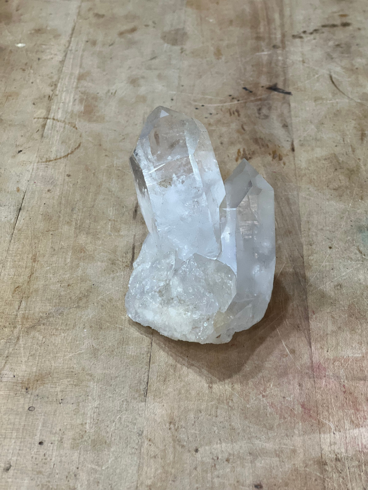 A natural clear quartz crystal cluster with rough and polished sections, resting on a weathered wooden surface.