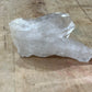 A rough, unpolished crystal cluster with natural faceted edges, resting on a textured wooden surface.