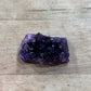 A raw amethyst crystal cluster with a dark purple cavity and faceted purple crystal points, resting on a light brown wooden surface.